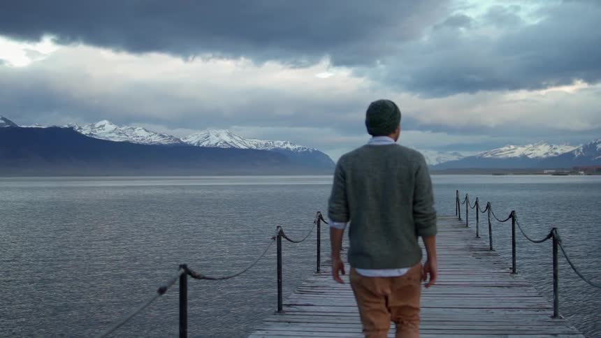 Man walks on a dock looking out at a large lake