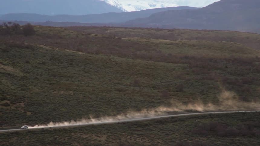 A vehicle drives down the road leaving dust behind