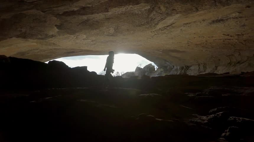 Woman walks in a cave towards the entrance on a sunny day