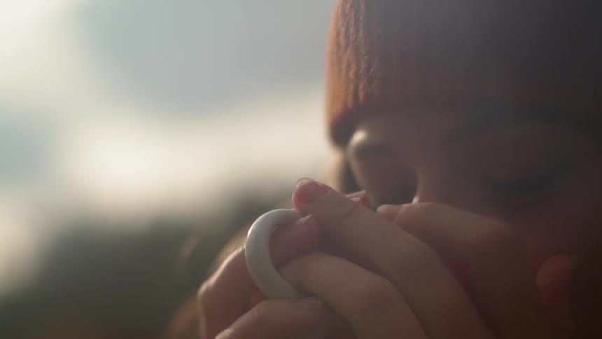 A woman drinks from a mug outside at sunset