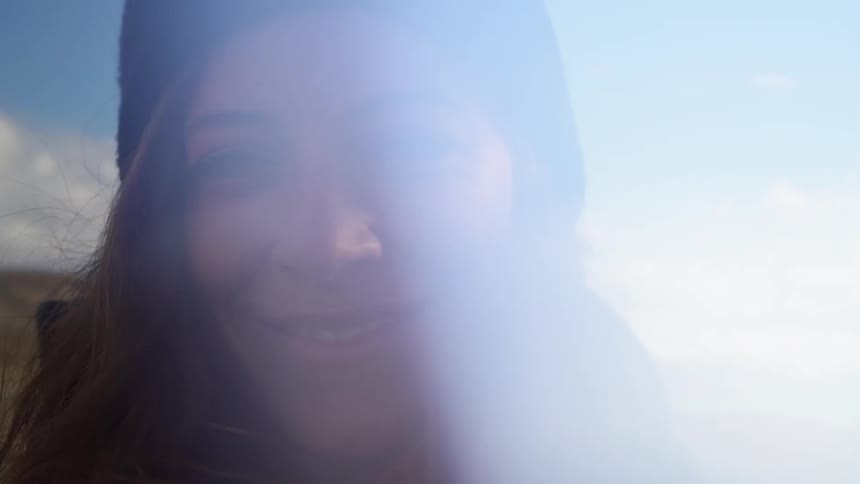 A woman is smiling as sunlight reflects on her while standing outside in a natural setting