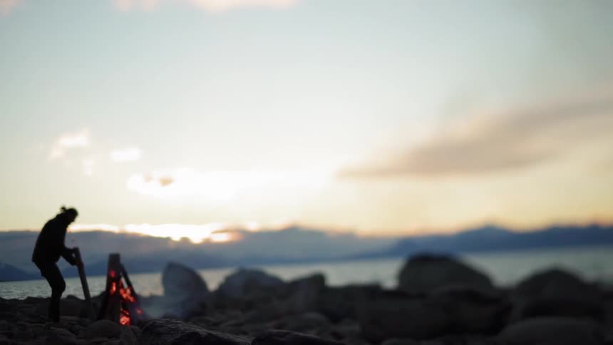A person builds a bonfire next to a lake at sunset