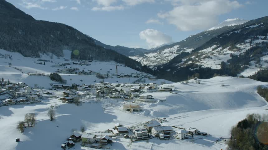 Snow is covering an alpine village on a mountain hillside in daylight