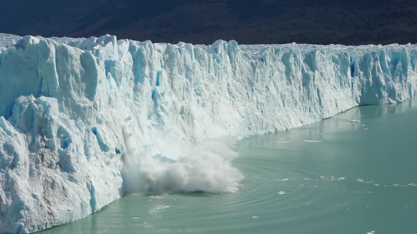 Large piles of snow from a cliff fall into a body of water