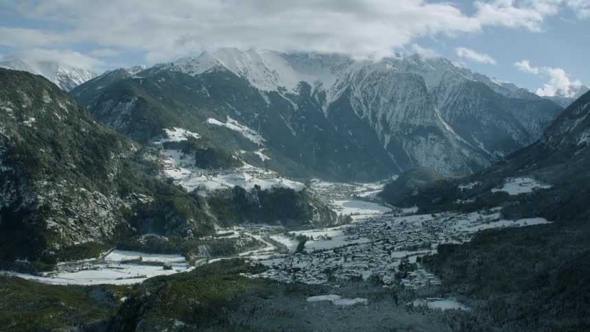 A village is sitting nestled in the valley of a mountain range in winter