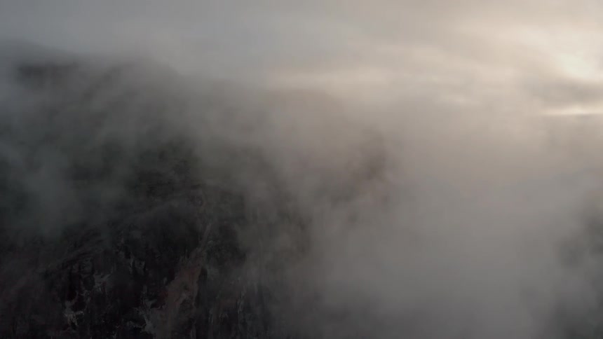 Clouds are drifting across snow-covered mountains during the day