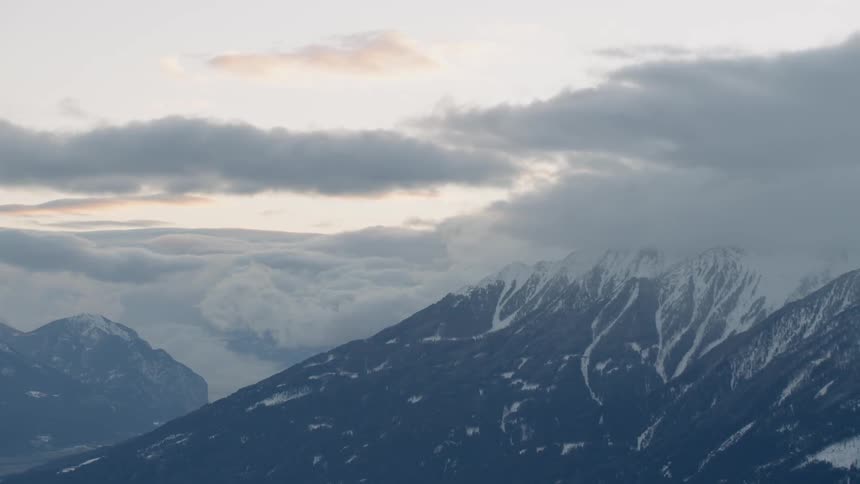 Clouds are drifting across snow-covered mountain peaks at dawn