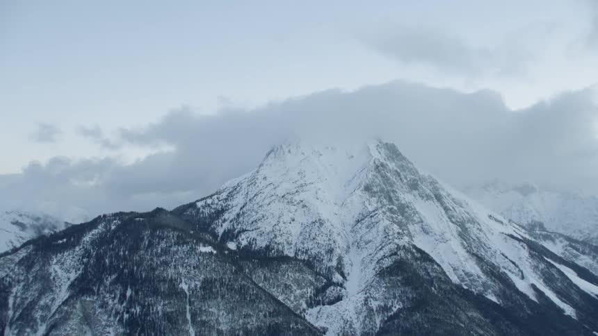 Clouds are drifting across snow-covered mountain peaks during the day