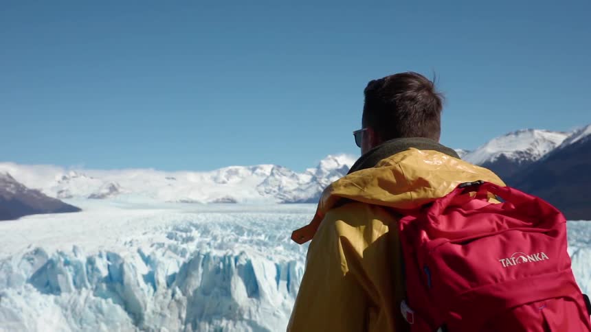 Man wearing a red backpack looks out over snowy terrain
