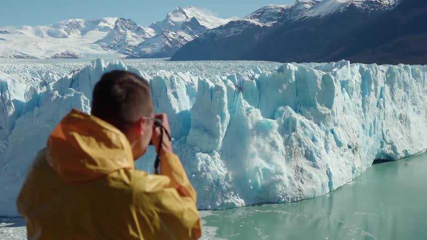 Man takes pictures of snow falling from large glacier