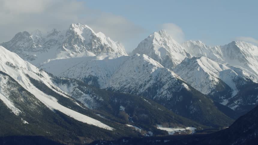 Clouds are drifting across snow-covered mountain peaks on a sunny day