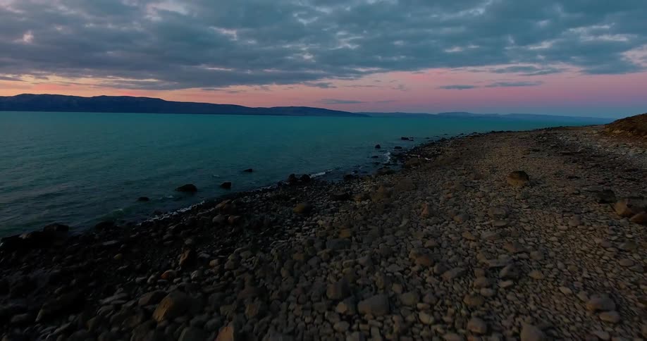 Friends are dancing at a campfire on a rocky beach at dusk