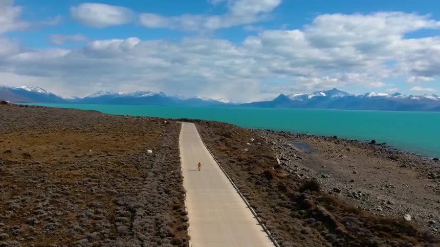 A person is riding a skateboard down the middle of a remote road during the day
