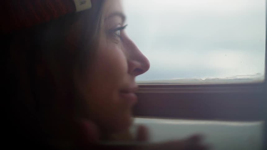 A woman blows on a cup of coffee and looks out a window