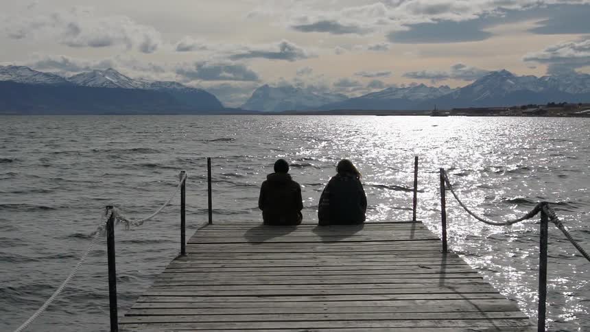 Two people sit at the end of a dock