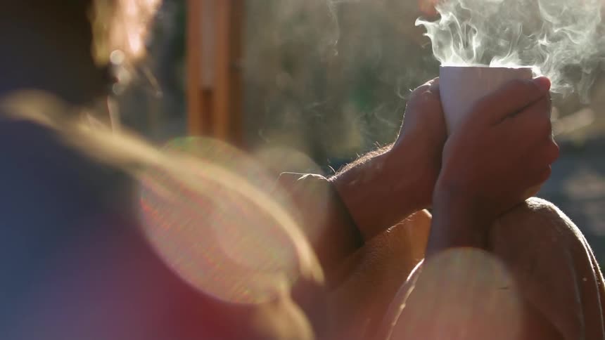 A man holds a steaming cup of coffee outside