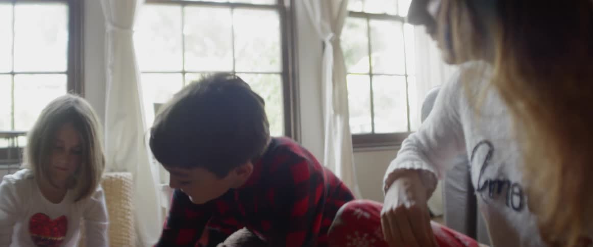 A woman is playing with three children on a living room floor in daylight