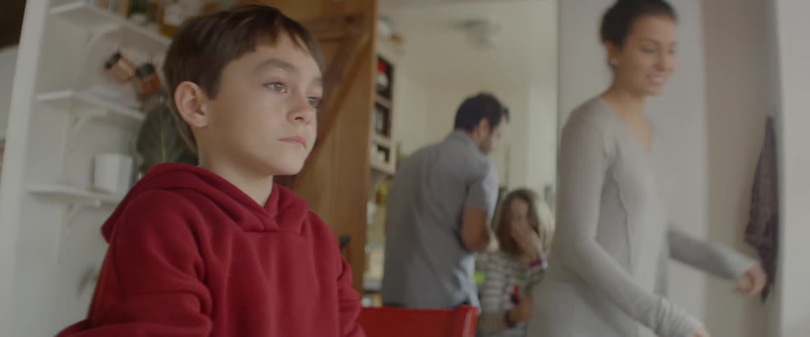 A child eats food in the dining room as the family clears up