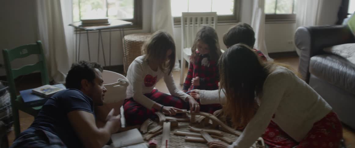 A family are playing with a toy track on their living room floor in daylight