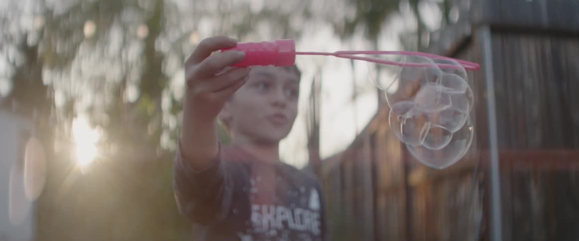 A boy is blowing bubbles in a backyard in daylight