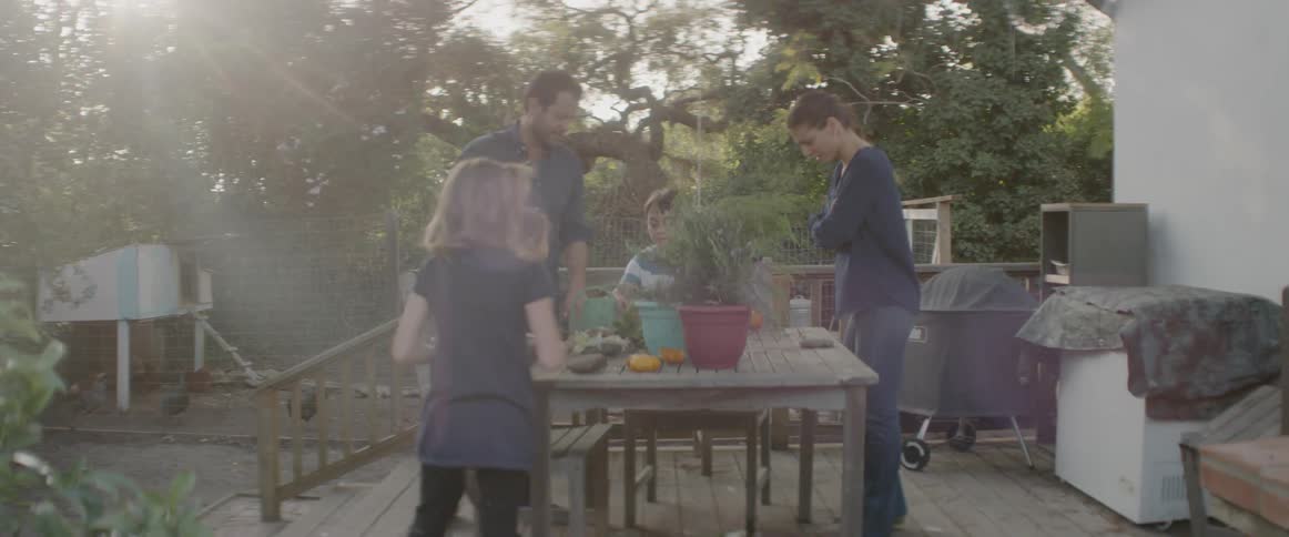 Family stands around a table outside on a deck