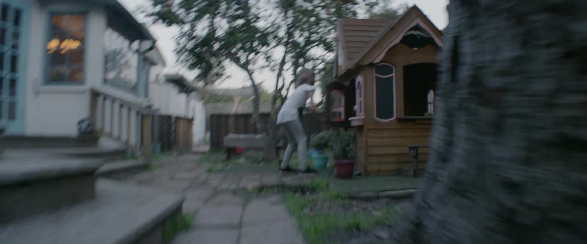 A girl is running through her backyard as she plays with her sibling at dusk