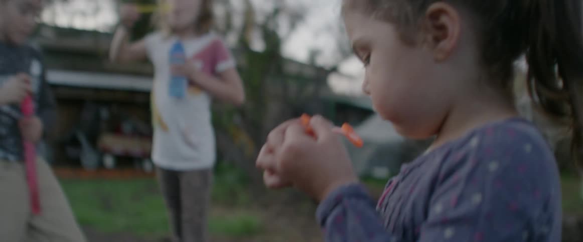 A girl and her siblings are blowing bubbles in a backyard in daylight