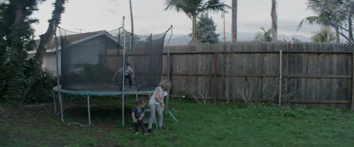 Children are getting off a trampoline as they play in their backyard at dusk