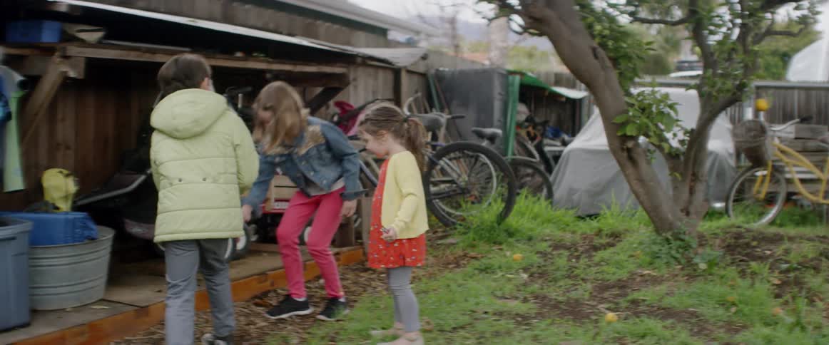 Children play outside in a yard near a shed full of bikes