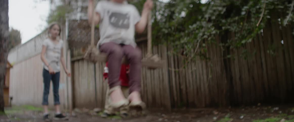 A boy and girl push another girl on a swing