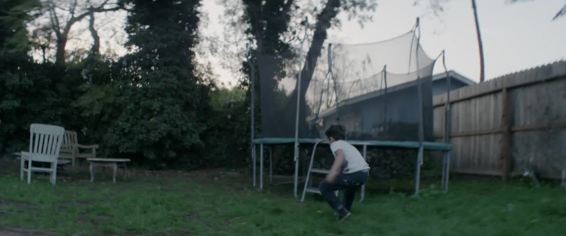 A boy is playing with a ball in a backyard at dusk