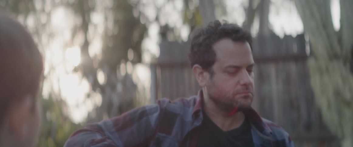 A boy watches a man play guitar in a backyard