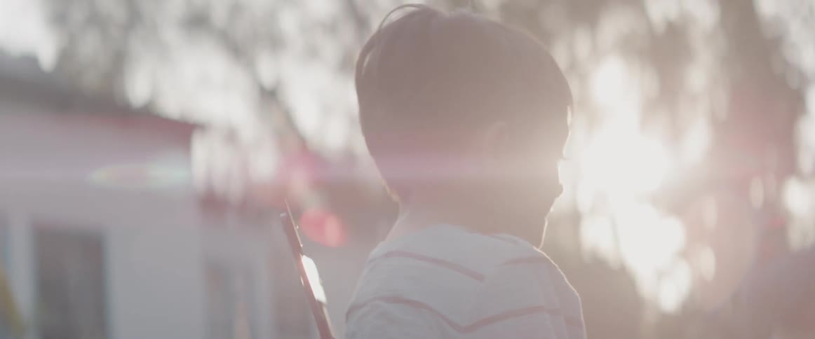 A boy is smiling as he watches his father play guitar in their backyard