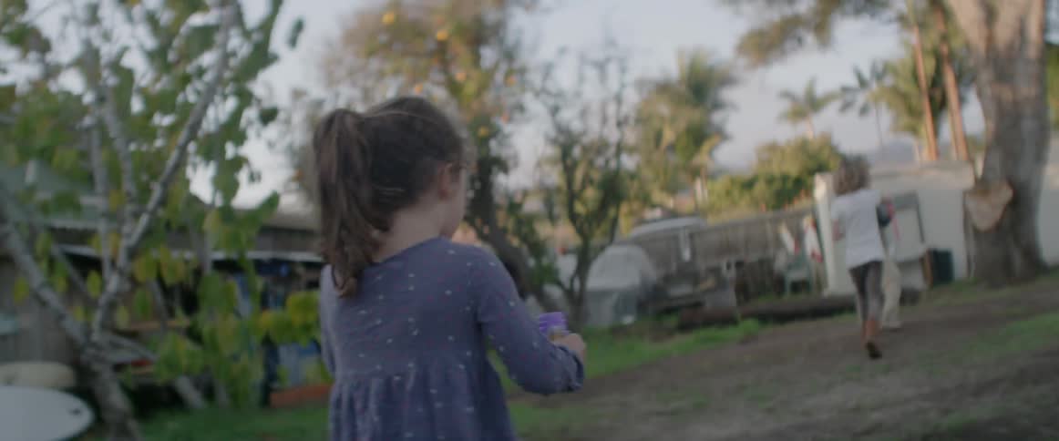 Little girl running in a backyard trying to blow bubbles while other children play