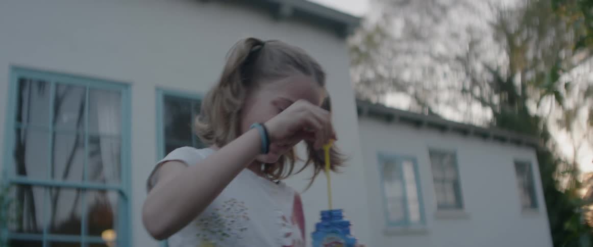 A girl smiles and blows bubbles outside at sunset
