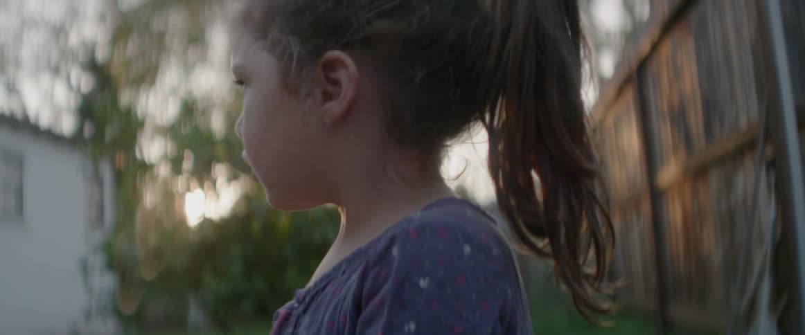 A girl is blowing bubbles in a backyard at dusk