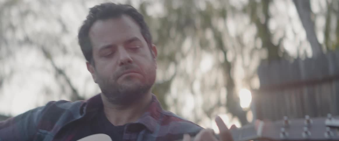A man sitting in the yard playing a guitar