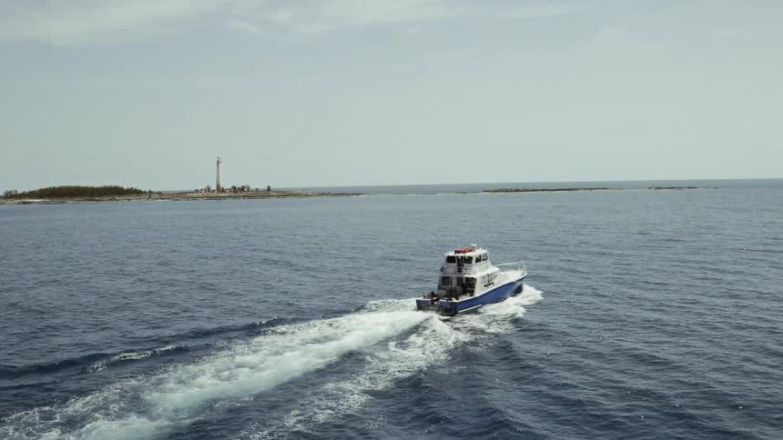 A boat is sailing out of a harbor past a lighthouse on a sunny day