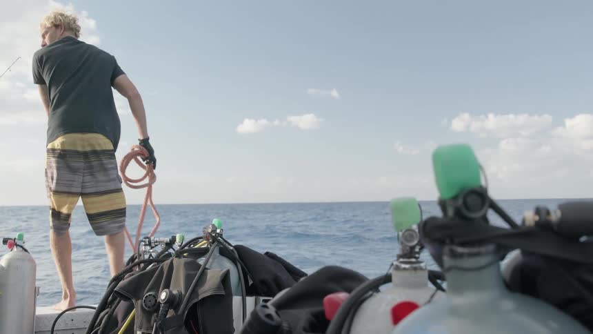 A man is holding a rope and balancing on the edge of a boat on a sunny day