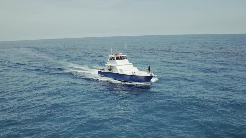 A man is standing on the prow of a boat as it sails during the day