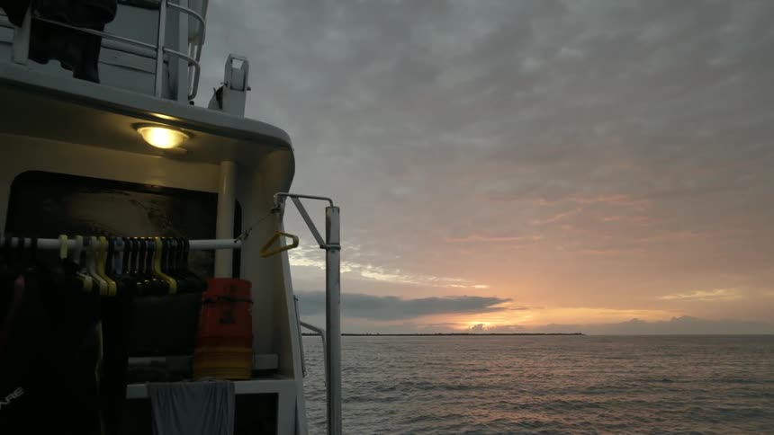 The boat is slowly moving in the water at sunset