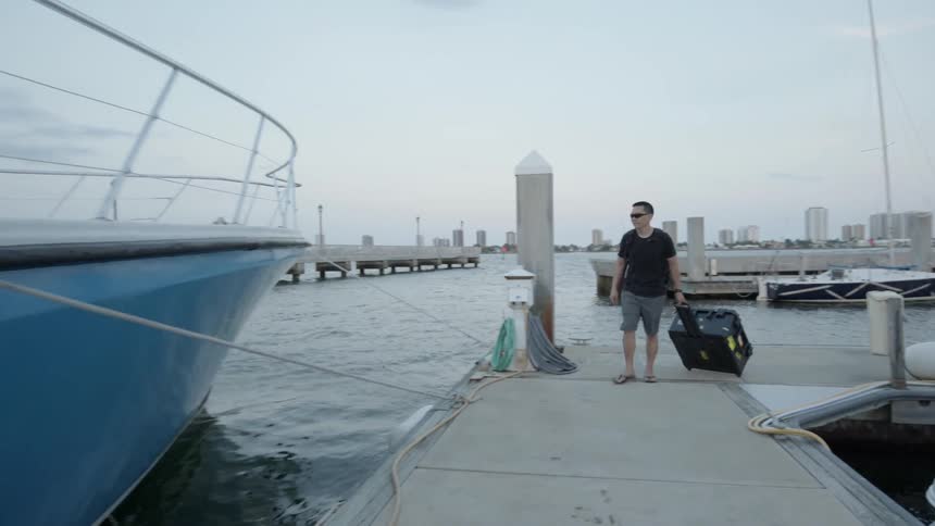 A man is dragging a case behind him as he walks toward a boat in daylight