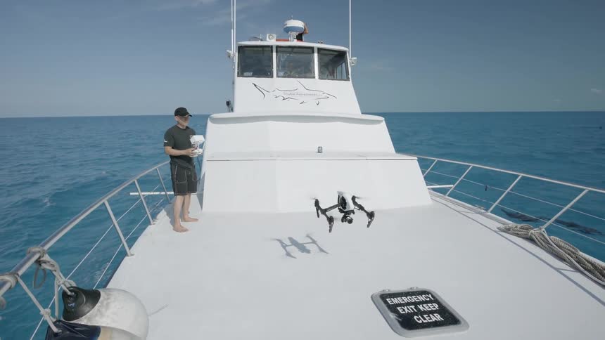 A man flies a drone on a ship sailing on the ocean