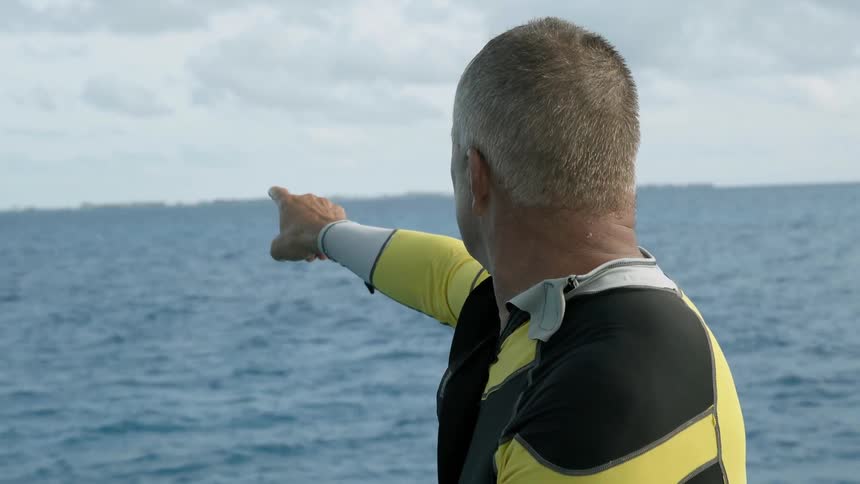 Man riding a boat points outward towards the water