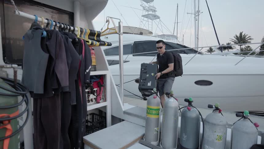 A man is carrying a heavy box as he boards a boat in daylight