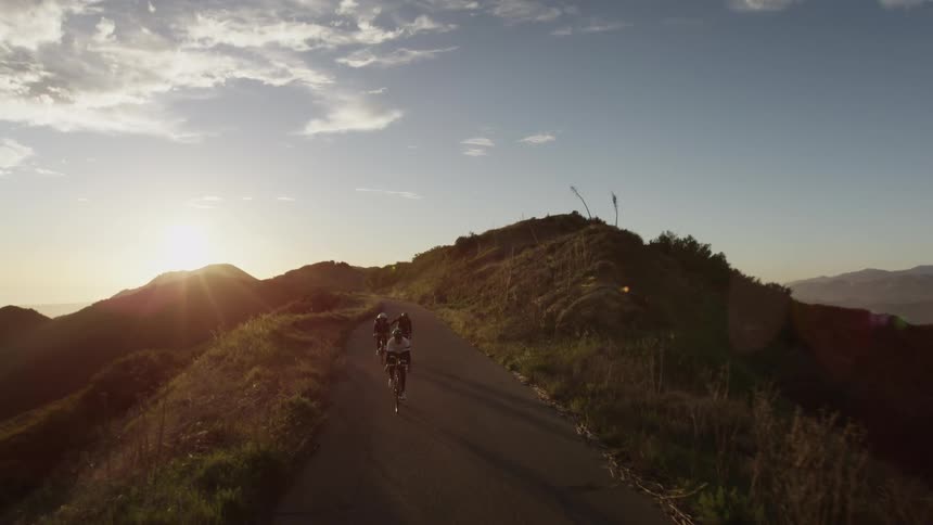 People riding ten speeds down a winding mountain road as the sun sets