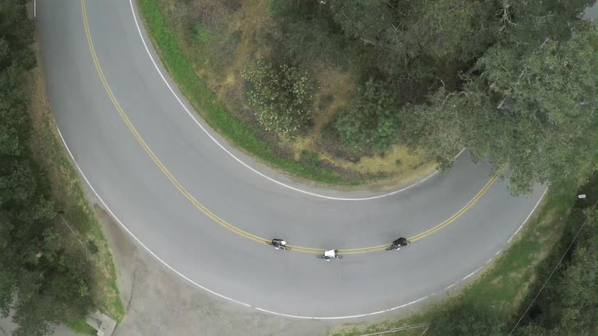 A very curvy road with three bikes riding down it
