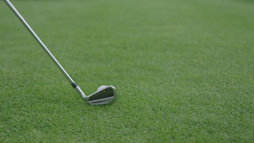 A golf club swings right up to a golf ball on a green and then stops