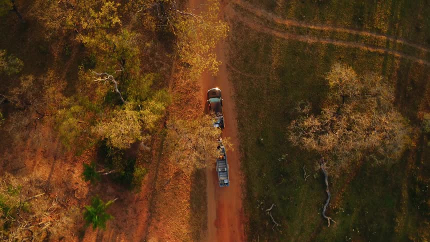 A pickup truck is towing a boat over a rural dirt road in daylight