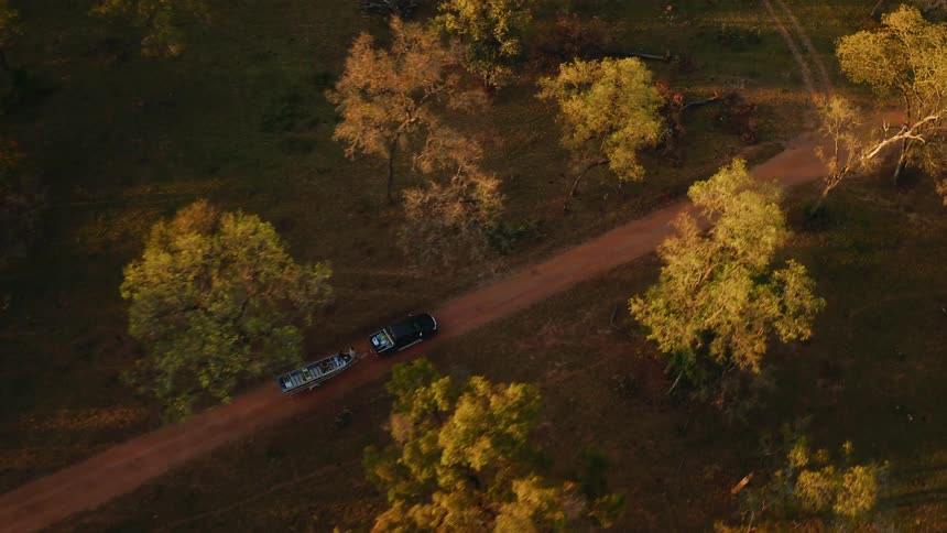 A truck pulls a boat on a rural dirt road